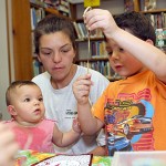Alivia Ruggiano, 9 months, helps her older brother, Robbie Ruggiano, 5, decorate a mask as their mother, Sarah Ruggiano, watches over July 14 at the Beacon Falls Public Library.